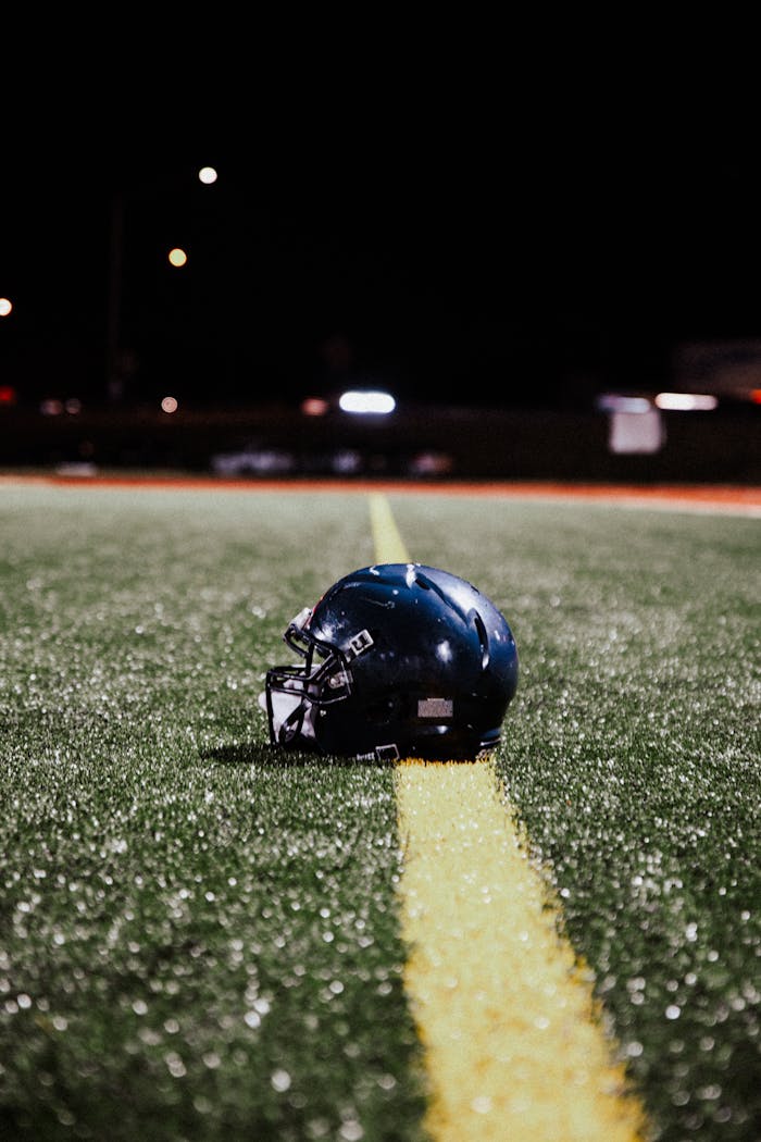 A lone American football helmet rests on a field under night lights.