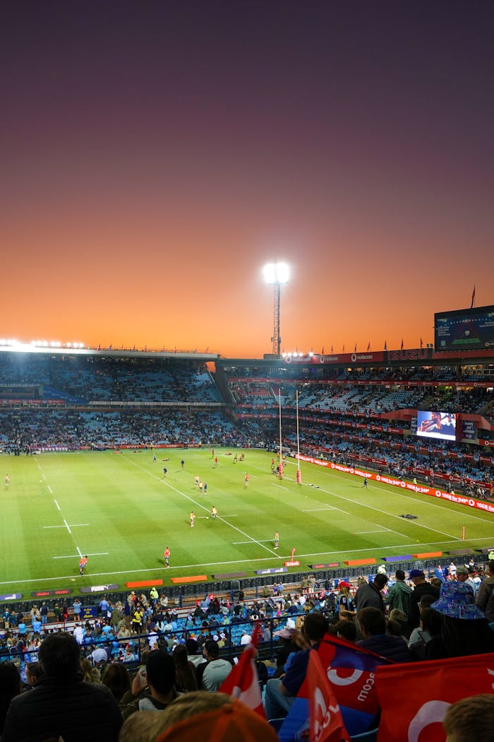 A vibrant rugby match taking place in a large stadium during sunset, with cheering crowd.