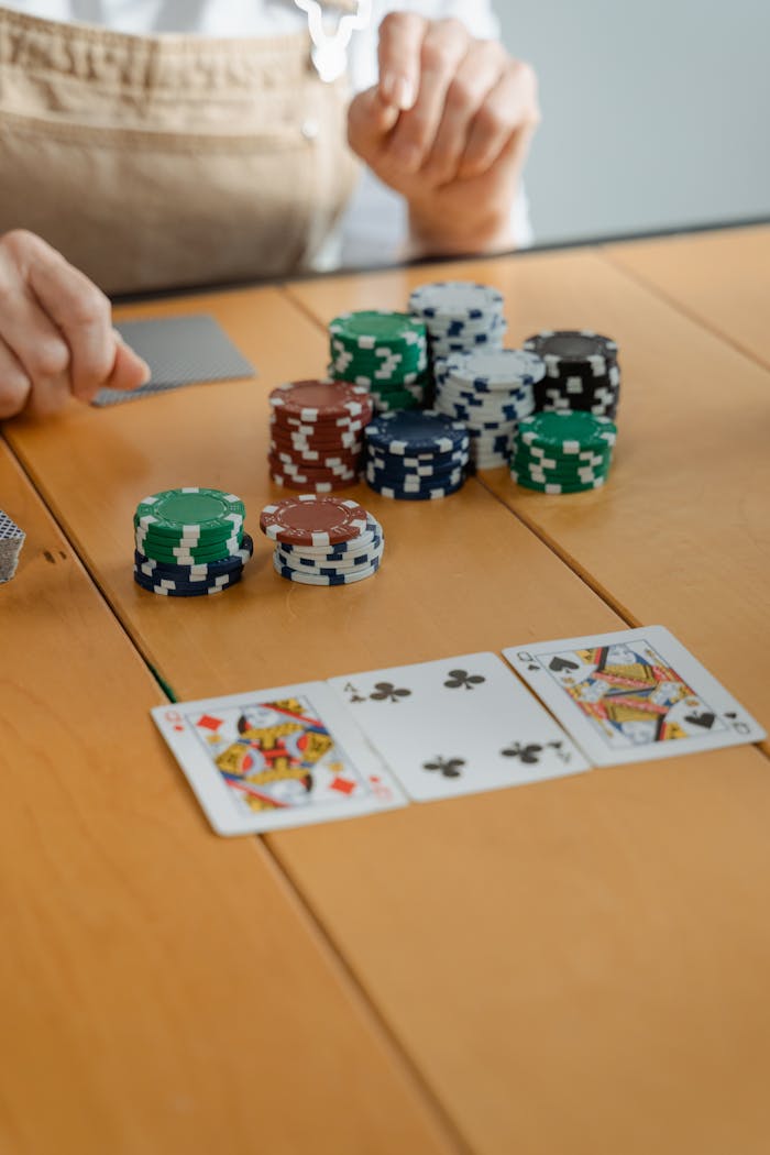 Elderly person engaging in poker game with chips and cards on a wooden table at home.